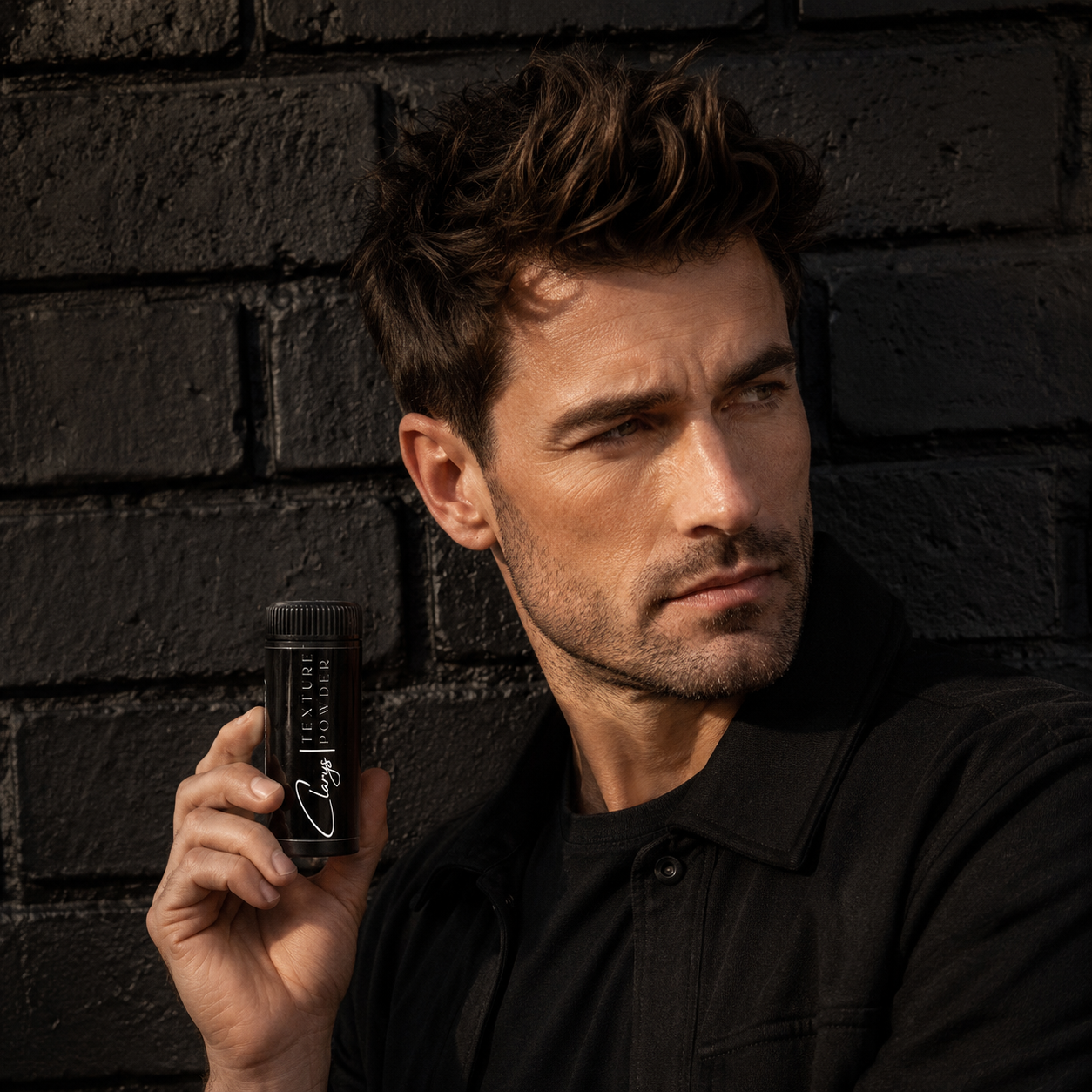 Man with volumized, textured hair holding Clary's Texture Powder against a brick wall